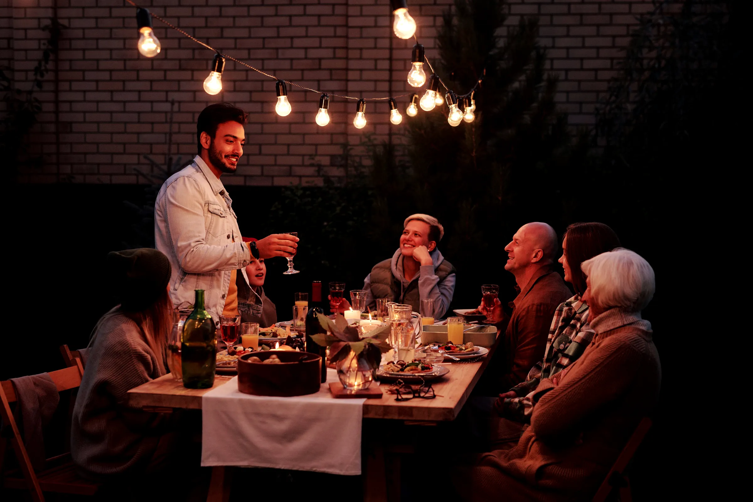 Friends sharing dinner at a long outdoor table under string lights